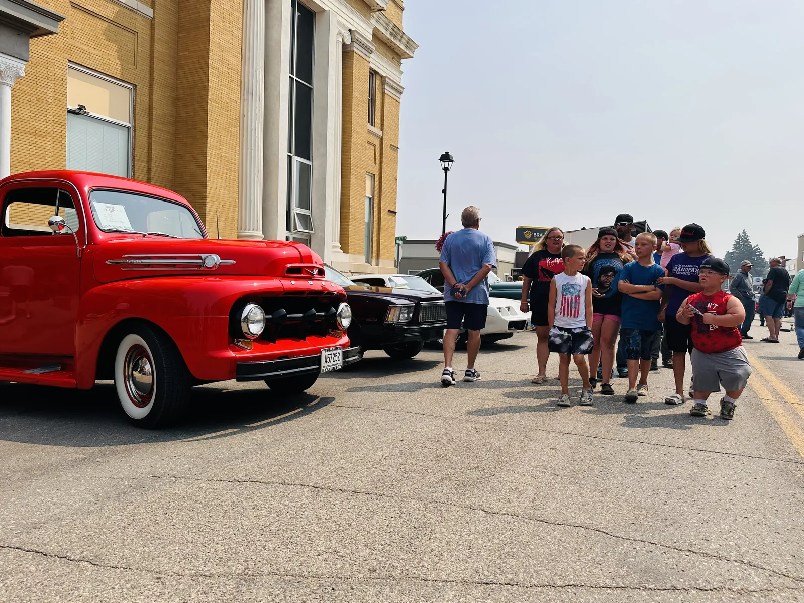Red vintage Ford truck parked on Main Street with a group of kids posing next to it