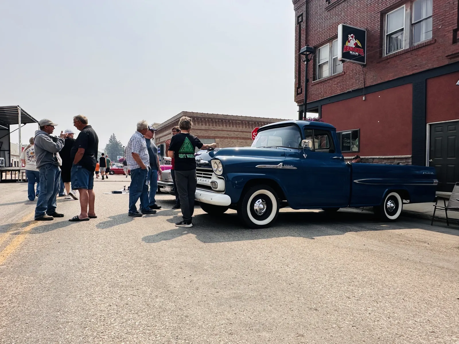 Classic blue Chevy Apache pickup truck on Main Street with owners chatting nearby