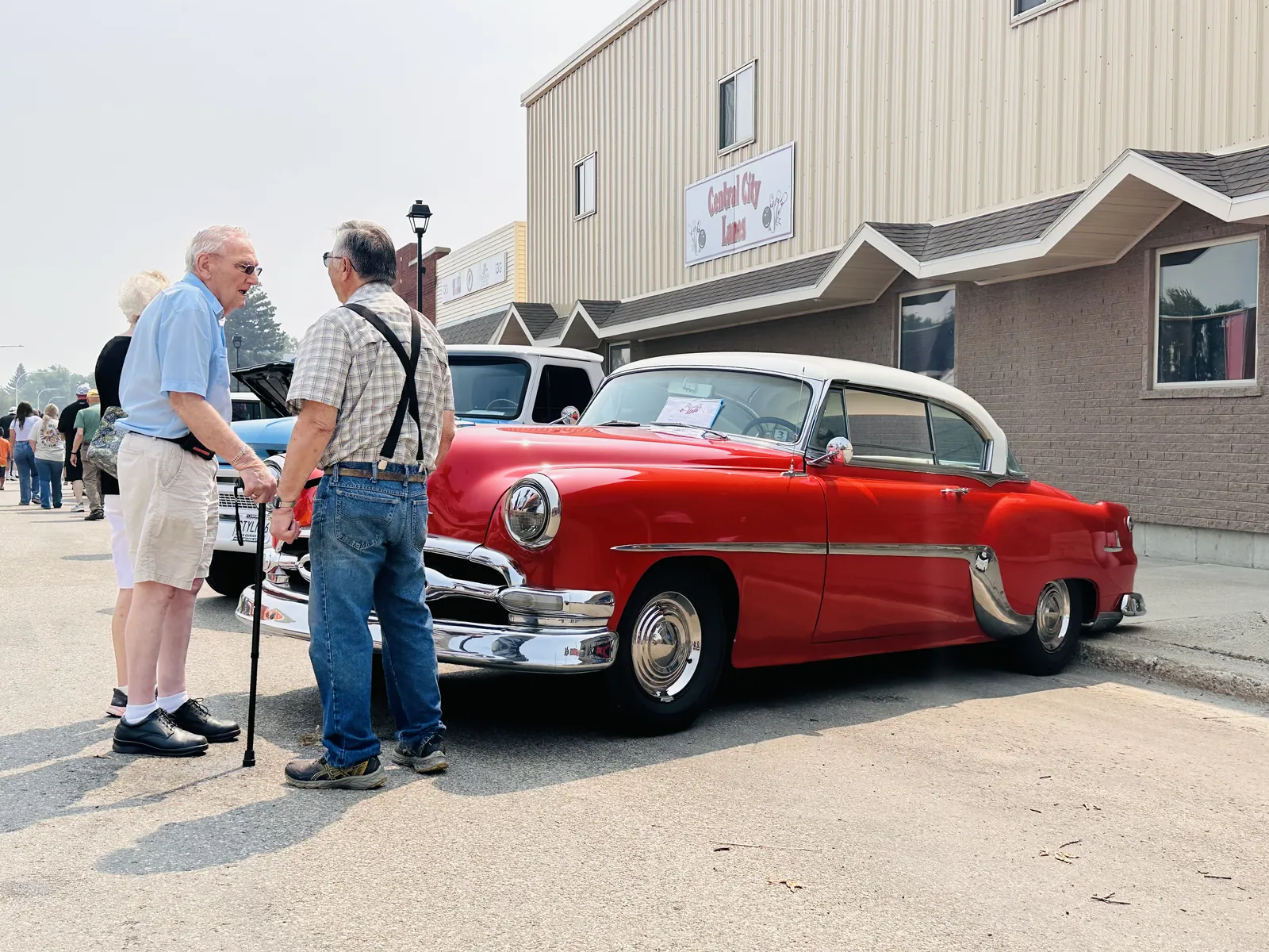 Bright red classic 1950s Chevrolet with two elderly men admiring it on Main Street