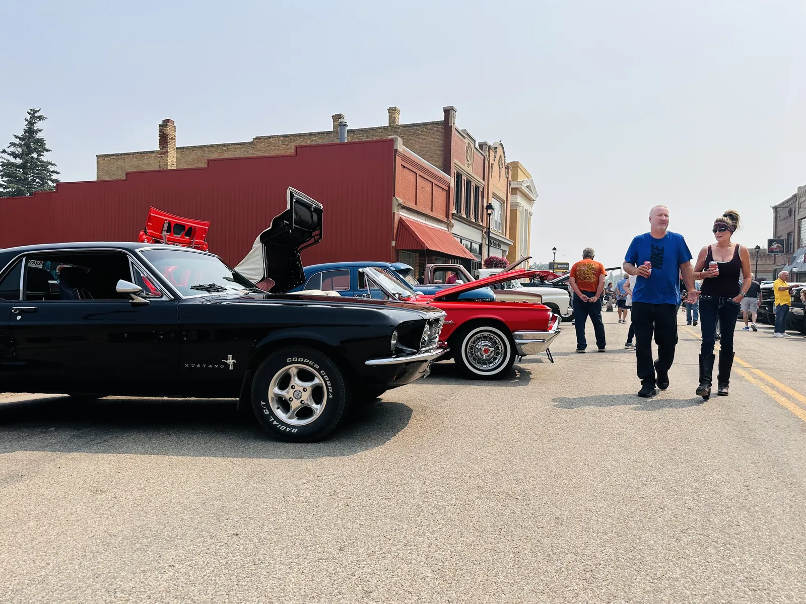 Black and red classic Ford Mustangs lined up on Main Street with a couple walking past
