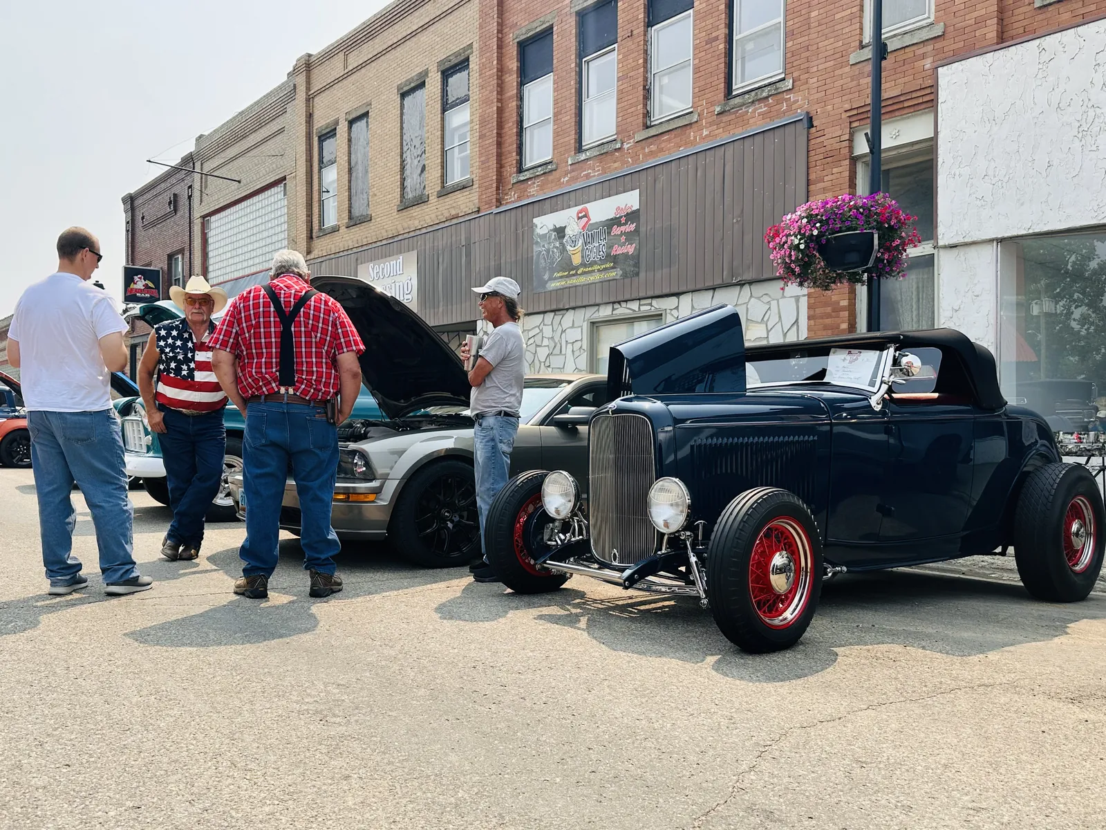 Black vintage hot rod roadster parked on Main Street with visitors admiring it