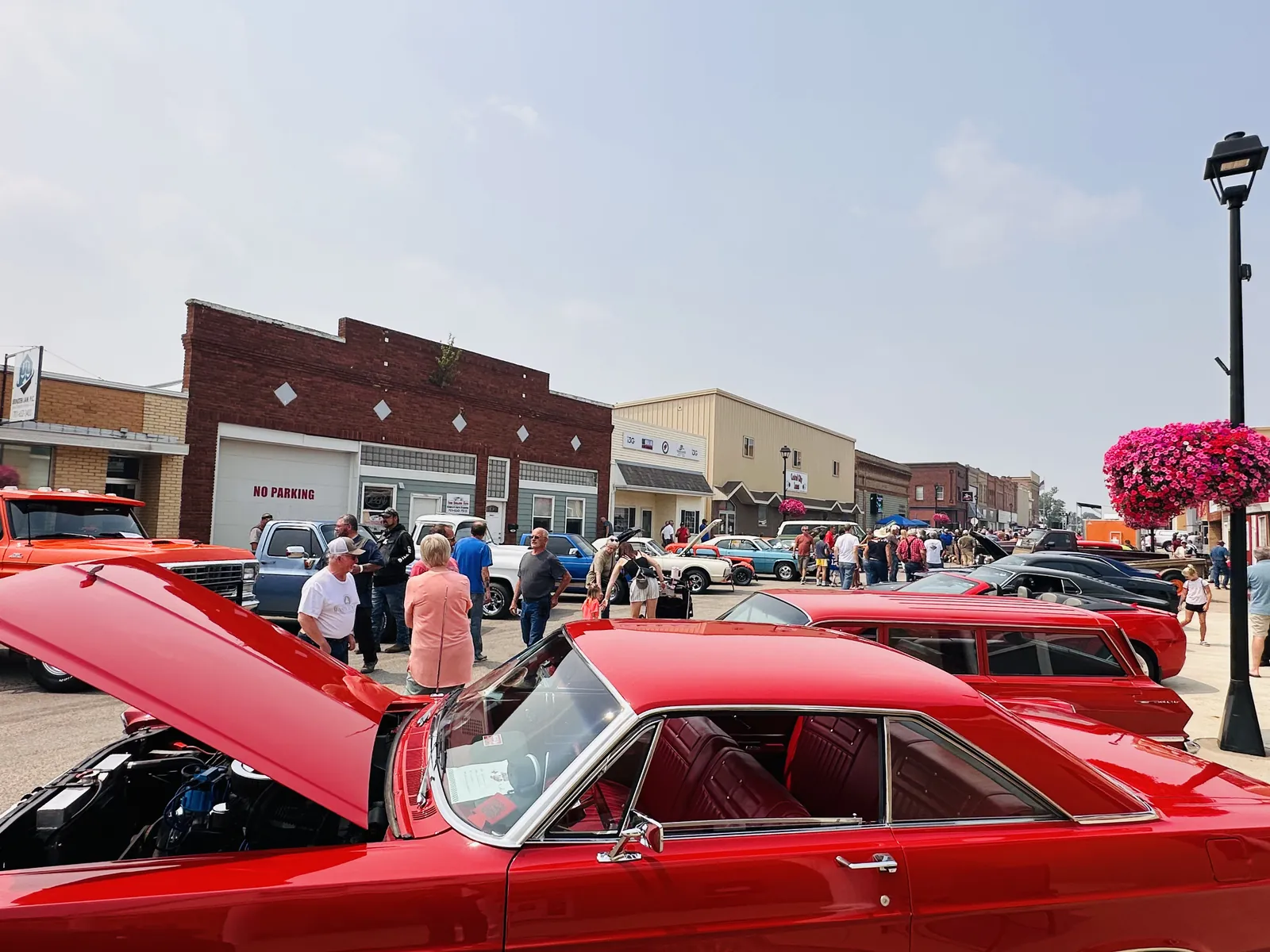 Red classic car with hood up on Main Street Carrington and crowds browsing the show